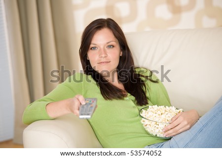 Woman watching television with popcorn in living room, holding remote control