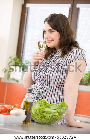 Cook - Plus size happy woman with white wine and lettuce in modern kitchen