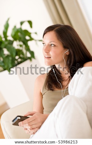 Woman holding music player listening with ear buds lying down on sofa home