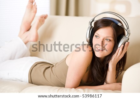 Happy woman with headphones lying down on sofa  in lounge, listen to music
