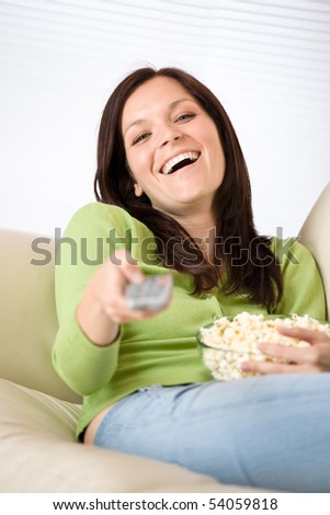 Woman pointing with television remote control  with popcorn in living room, holding remote control