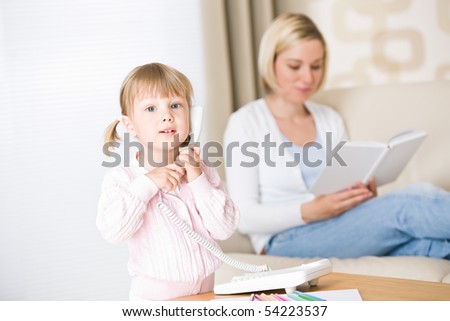 Little girl on phone in living room, mother in background