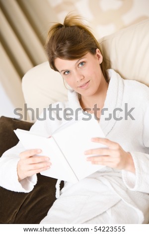 Young woman read book on sofa relaxing in lounge wearing bathrobe