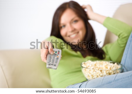 Woman watching television with popcorn in living room, holding remote control