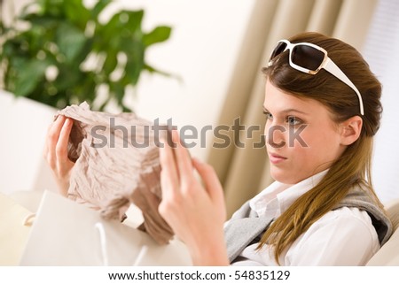 Young businesswoman unpacking shopping bag on sofa, plant in background