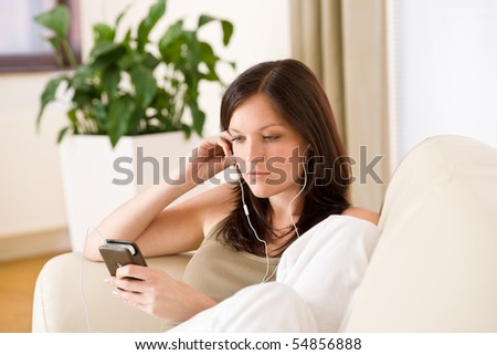Woman holding music player listening with earbuds home, plant in background