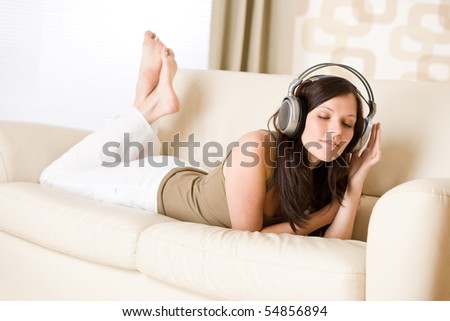 Happy woman with headphones lying down on sofa  in lounge, listen to music