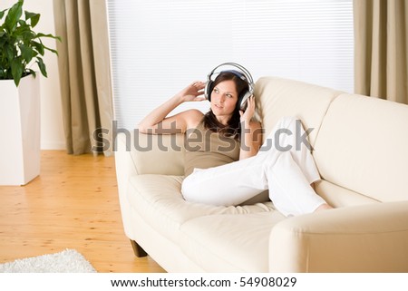 Woman with headphones listen to music  in lounge, plant in background