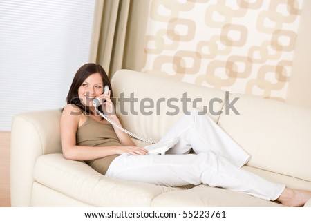 On the phone home - Smiling woman lying down on sofa calling
