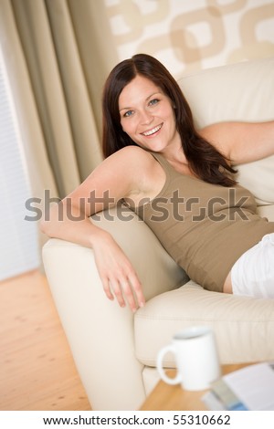 Young woman with magazine and coffee in lounge on sofa