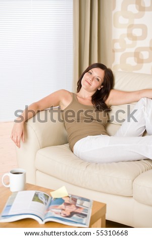 Young woman with magazine and coffee in lounge relaxing on sofa