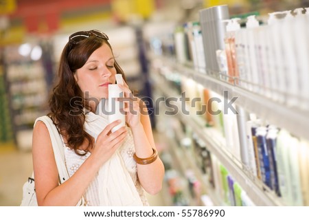 Shopping cosmetics - woman smelling bottle of shampoo in supermarket
