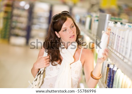 Shopping - thoughtful woman looking at bottle of shampoo in supermarket