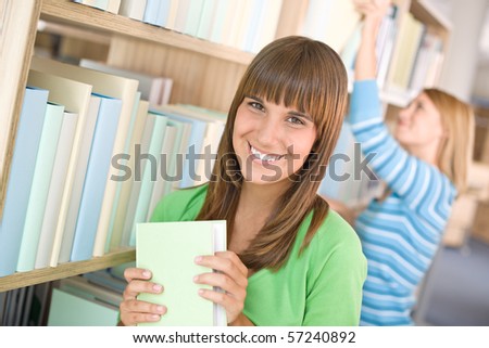 Student in library - two woman choose book from bookshelf