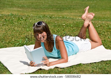 Smiling young woman read book in park on sunny day sitting on blanket