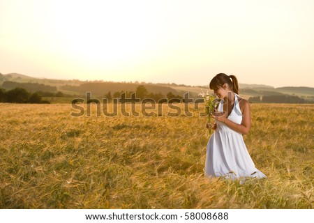 Romantic brunette woman in sunset corn field wear white dress, holding bouquet of flowers
