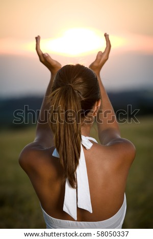 Young brunette woman in sunset with hands up