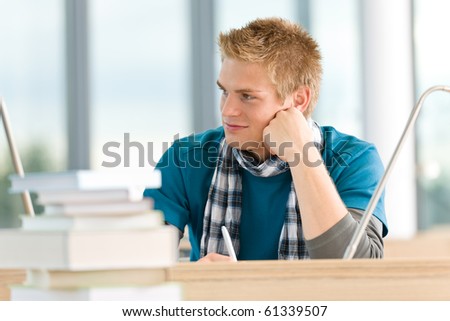 Male student with books sitting at table at high school