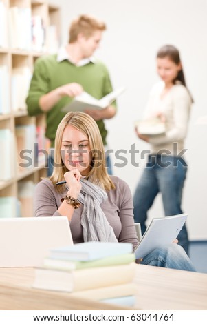 High school library - thoughtful female student with laptop and book