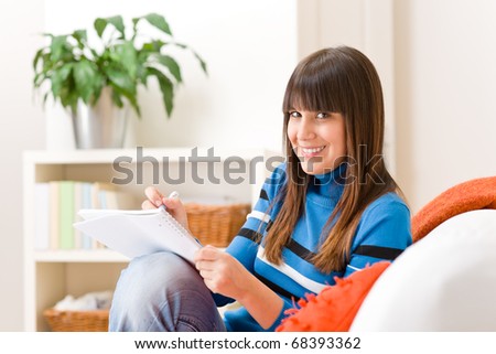 Teenager girl home - student write homework sitting on sofa