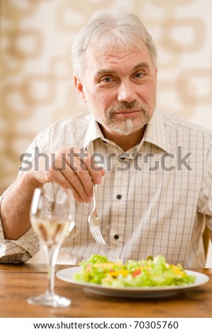 Senior mature man eat vegetable salad and white wine at wooden table
