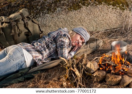 Young hiking woman with backpack sleep by campfire countryside