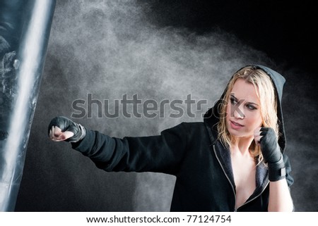Blond boxing woman in black training with punching bag