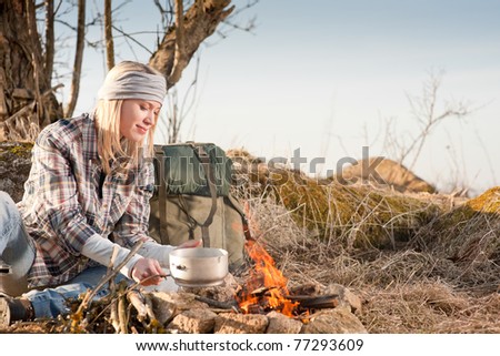 Young hiking woman with backpack cook on campfire in countryside