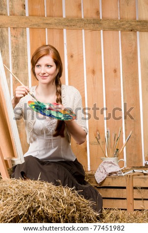 Young red-hair romantic woman with color palette painting in barn