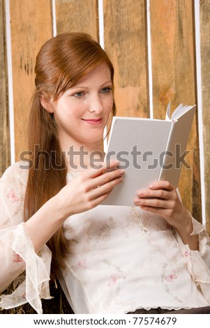 Young romantic red-hair woman reading book sitting in barn country