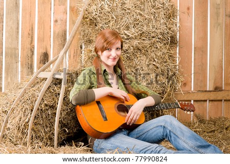 Young country woman sitting on hay with guitar in barn