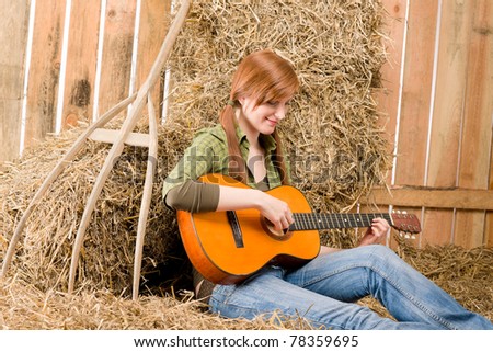 Young country woman sitting on hay play guitar in barn