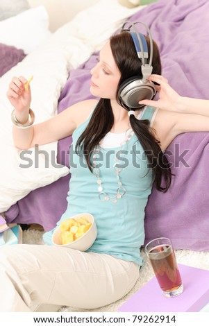 Young happy girl relax listen to music eat chips