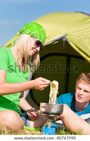 Young camping couple cooking meal outside tent in sunny countryside