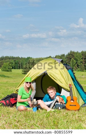 Young camping couple cooking meal outside tent in sunny countryside