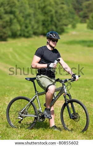Fit young cycling man relax with water bottle in summer countryside