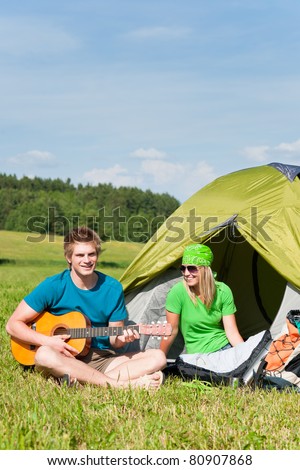 Happy camping couple sitting by tent play guitar sunny countryside