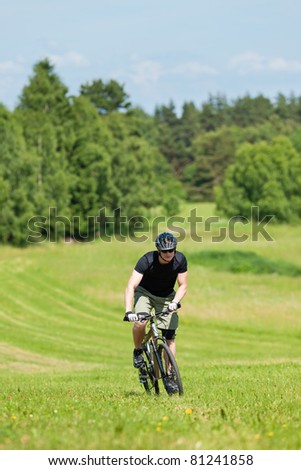 Fit young man cycling uphill mountain bike in summer countryside