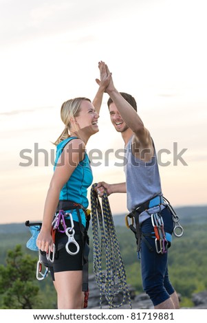 Rock climbing cheerful active young mountaineers reach top at sunset