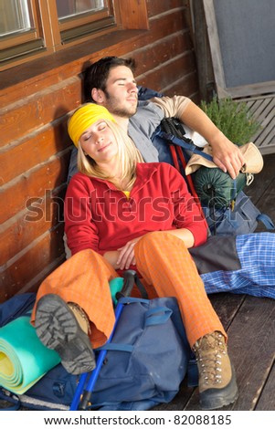 Tramping young couple backpack sleep sitting by wooden cottage