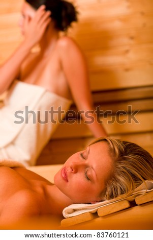 Sauna two healthy beautiful women relaxing sweating lying covered towels