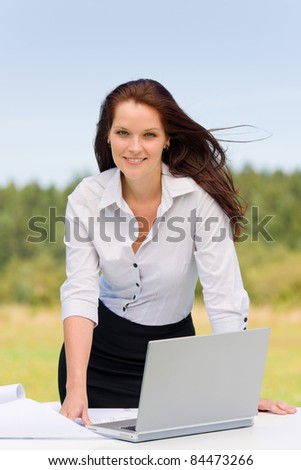 Young businesswoman in sunny nature with laptop behind table smiling