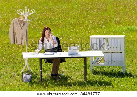 Young businesswoman in sunny meadow nature office calling behind table