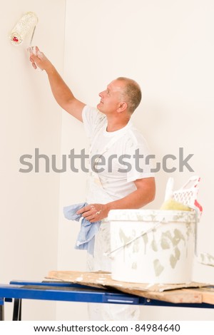 Home decorating mature man painting white wall with roller
