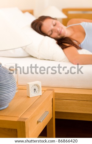 Alarm clock on bedside table woman sleeping in white bed