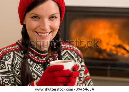 Winter Christmas woman with hat and gloves drink by fireplace