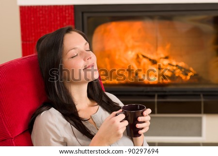 Young woman enjoying winter hot drink relax by home fireplace