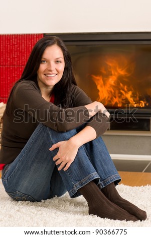 Beautiful happy young woman sitting front of home fireplace