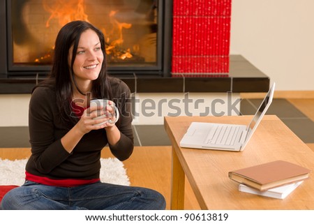 Happy woman at fireplace with laptop enjoying winter hot drink