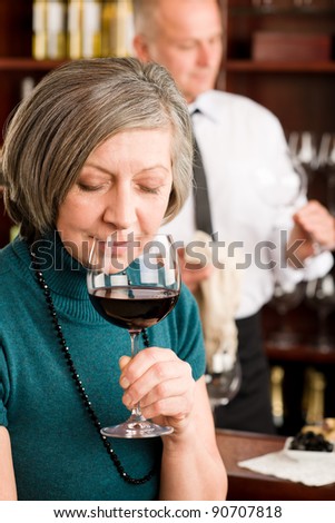 At the bar - happy senior woman taste red wine glass